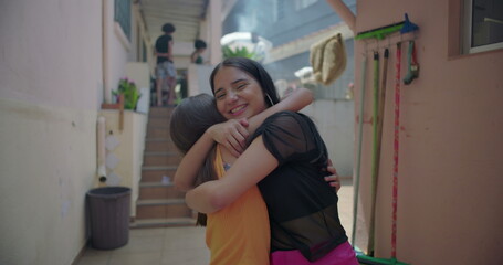 Two young Hispanic Latin girls hugging and laughing in suburban alleyway, joyful and playful...