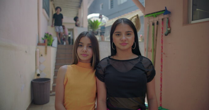 Two young Hispanic Latin girls hugging and laughing in suburban alleyway, joyful and playful moment, representing friendship and multicultural identity