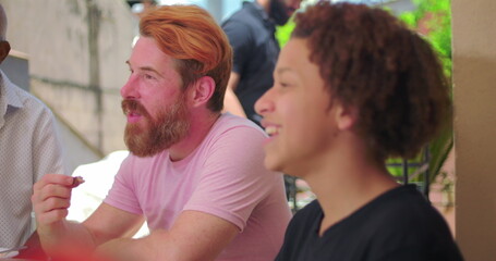 Hispanic Latin teenager of African descent laughing joyfully while engaging with others during a lively outdoor family meal, capturing energy and connection