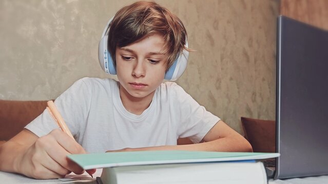 Boy Uses Laptop for Learning, Writes Down Useful Information. Distance Learning, e-Education, Homeschooling Concept. Portrait of a Boy Doing Homework