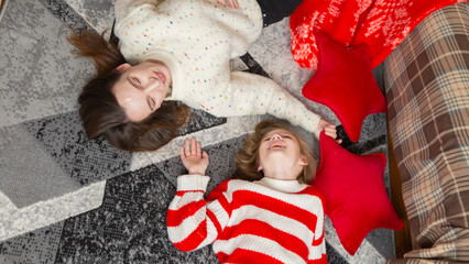 Funny happy mother and daughter having fun laughing rejoicing in anticipation of Christmas lying on...