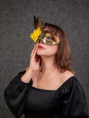Portrait of a beautiful woman of 40-50 years old wearing a golden carnival mask and a black dress