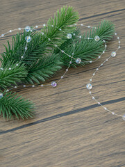 Green Christmas tree branch with a string of clear beads on a wooden table