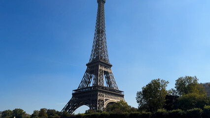 Eiffel Tower in Paris daytime view with clear blue sky, green trees at base, symbol of culture and travel.
