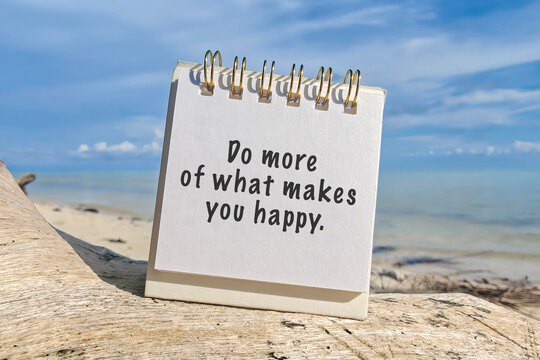 Motivational quote on notepad with text 'Do more of what makes you happy' placed on driftwood at the beach with blue sky and sea background. - Powered by Adobe