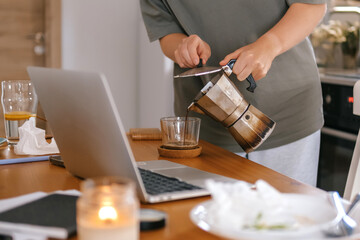  Gen Z woman working from home at cozy kitchen table with laptop and phone. Digital nomad lifestyle, mindfulness, remote work, balance, mental calm and modern freelancing