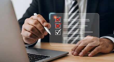 Man using a pen to fill out a digital checklist on a transparent screen near a laptop on desk