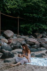 Caucasian young woman breastfeeding baby on rocky beach with lush greenery