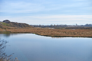 Tranquil rural landscape with calm river and distant hills under clear blue sky.