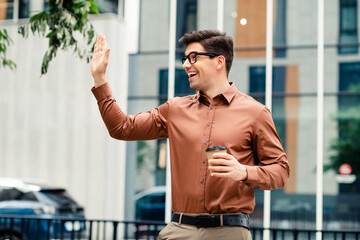 Professional young man greeting someone outdoors in an urban cityscape, holding a cup of coffee, dressed in smart casual attire