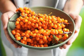 Woman with ripe sea buckthorn berries against blurred green background, closeup