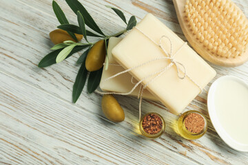 Natural soap bars with olives, brush, oil and green leaves on white wooden table, flat lay. Space for text