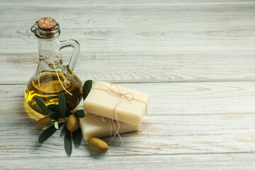 Natural soap bars with olives, oil and green leaves on white wooden table. Space for text