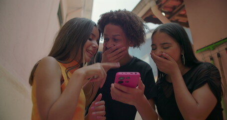 Teenagers laughing and pointing at smartphone screen in suburban alleyway, fun and interactive moment showcasing friendship, digital engagement, and youthful joy