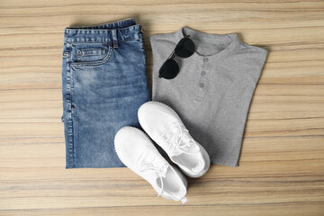 Grey t-shirt, jeans, sunglasses and sneakers on wooden table, flat lay. Mockup for design