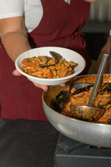 A chef in an apron presents a plate of pasta with seafood during food festival in Puglia