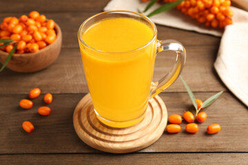 Cup of sea buckthorn tea and fresh berries on wooden table, closeup