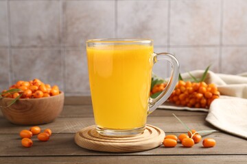 Cup of sea buckthorn tea and fresh berries on wooden table, closeup
