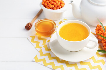 Sea buckthorn tea in cup, honey and fresh berries on white wooden table, closeup. Space for text