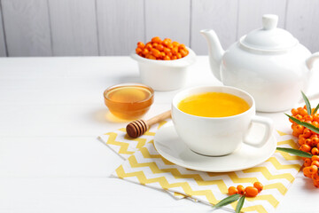 Sea buckthorn tea in cup, honey and fresh berries on white wooden table. Space for text