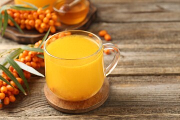 Sea buckthorn tea in cup and fresh berries on wooden table, closeup. Space for text