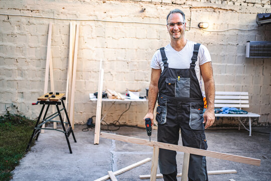 Mature male carpenter using electric screwdriver on a wooden plank outdoors