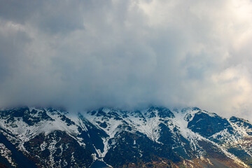 Snow-covered mountains partially obscured by clouds in daytime