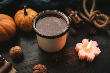 Cozy autumn scene with mug of hot chocolate, pumpkins, spices and candles on rustic dark wooden background, warm seasonal atmosphere