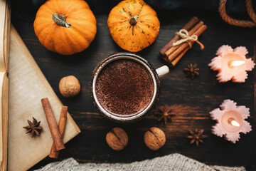 Fototapeta premium Cozy autumn scene with mug of hot chocolate, pumpkins, spices and candles on rustic dark wooden background, warm seasonal atmosphere, top view