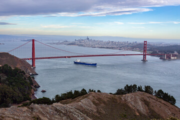 A cargo ship sails under the Golden Gate Bridge, connecting San Francisco to Marin County, facilitating trade and transportation.