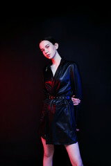 A young woman model in a dress in a photo studio on a black background with red light