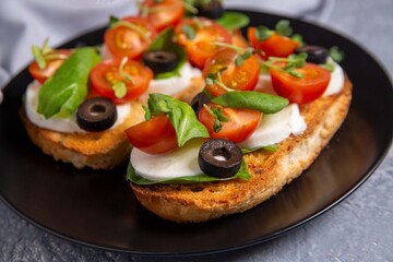 Bruschetta with cherry tomatoes, mozzarella cheese, olives and herbs. Italian Cuisine. Healthy eating.