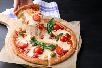 Woman taking piece of delicious pizza with cheese, tomatoes and olives at black wooden table, closeup