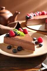 Piece of tasty chocolate cheesecake with berries served on wooden table, closeup