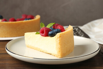 Piece of delicious cheesecake with fresh berries and mint on wooden table, closeup