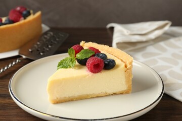 Piece of delicious cheesecake with fresh berries and mint served on wooden table, closeup