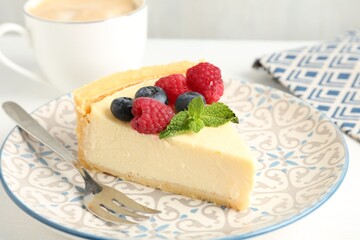 Piece of delicious cheesecake with fresh berries and mint served on white table, closeup