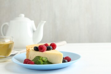 Piece of delicious cheesecake with fresh berries and mint served on white wooden table, space for text