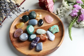 Different beautiful gemstones, flowers and book on white table, above view