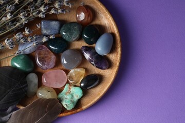 Different beautiful gemstones, feathers and lavender flowers on purple background, top view. Space for text