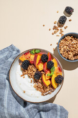 Natural greek yogurt with granola or muesli, peach and blackberry in a bowl on a beige background