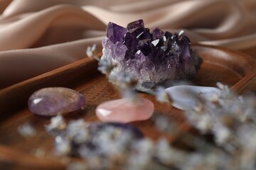 Different beautiful gemstones and lavender flowers on beige cloth, selective focus