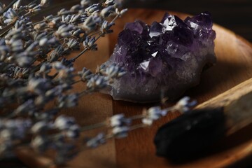 Beautiful amethyst gemstone, lavender flowers and palo santo stick on wooden plate, closeup