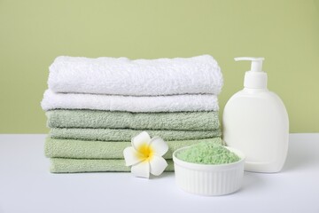 Stack of fresh terry towels, cosmetic products and plumeria flower on color background