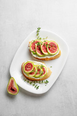 Toasts with fresh figs, cheese, thyme, and honey on a light background.