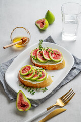 Sweet toasts with fresh figs, cheese, thyme, and honey on a light background.