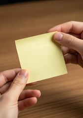 Obraz premium Hands holding blank yellow sticky note for creative reminders and important tasks at wooden table
