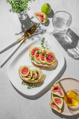 Sweet toasts with fresh figs, cream cheese, thyme, and honey on a light background.
