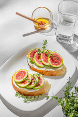 Sweet toasts with fresh figs, cream cheese, thyme, and honey on a light background.