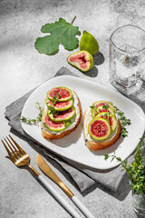 Sweet toasts with fresh figs, cream cheese, thyme, and honey on a gray background.